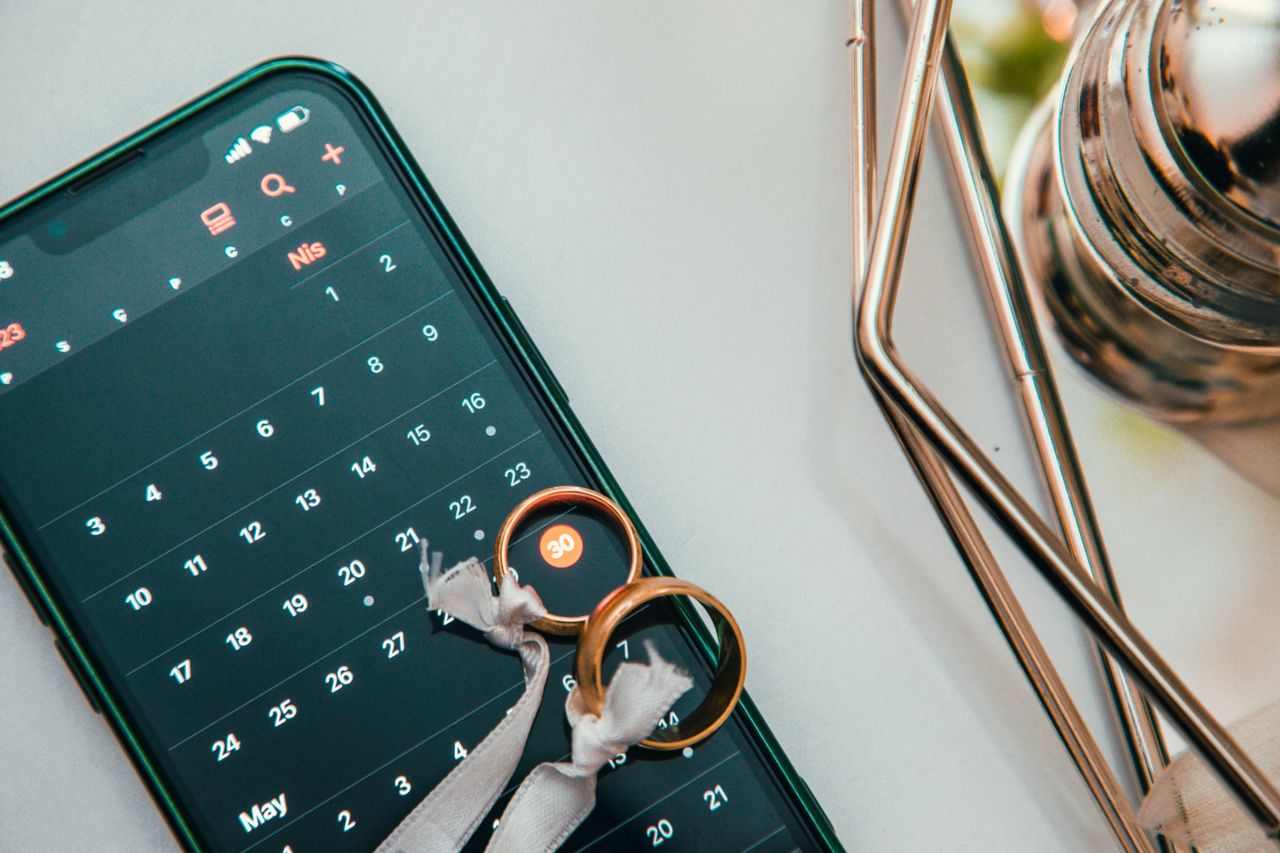Mastering the First Impression: Your intriguing post title goes here Elegant setup of wedding rings on a smartphone displaying a calendar date, symbolizing planning and celebration.
